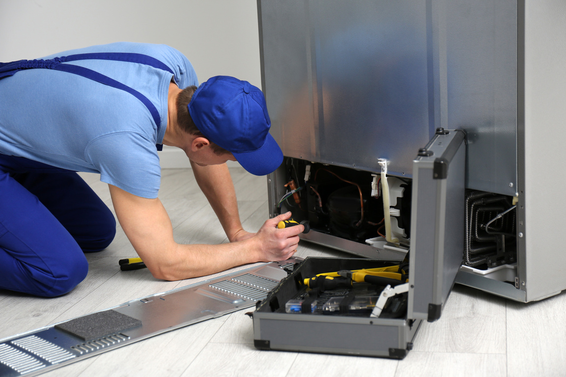 Male Technician with Screwdriver Repairing Refrigerator Indoors